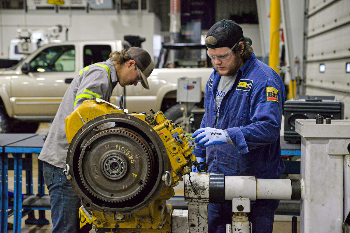 Two male students working on an engine in a garage classroom.